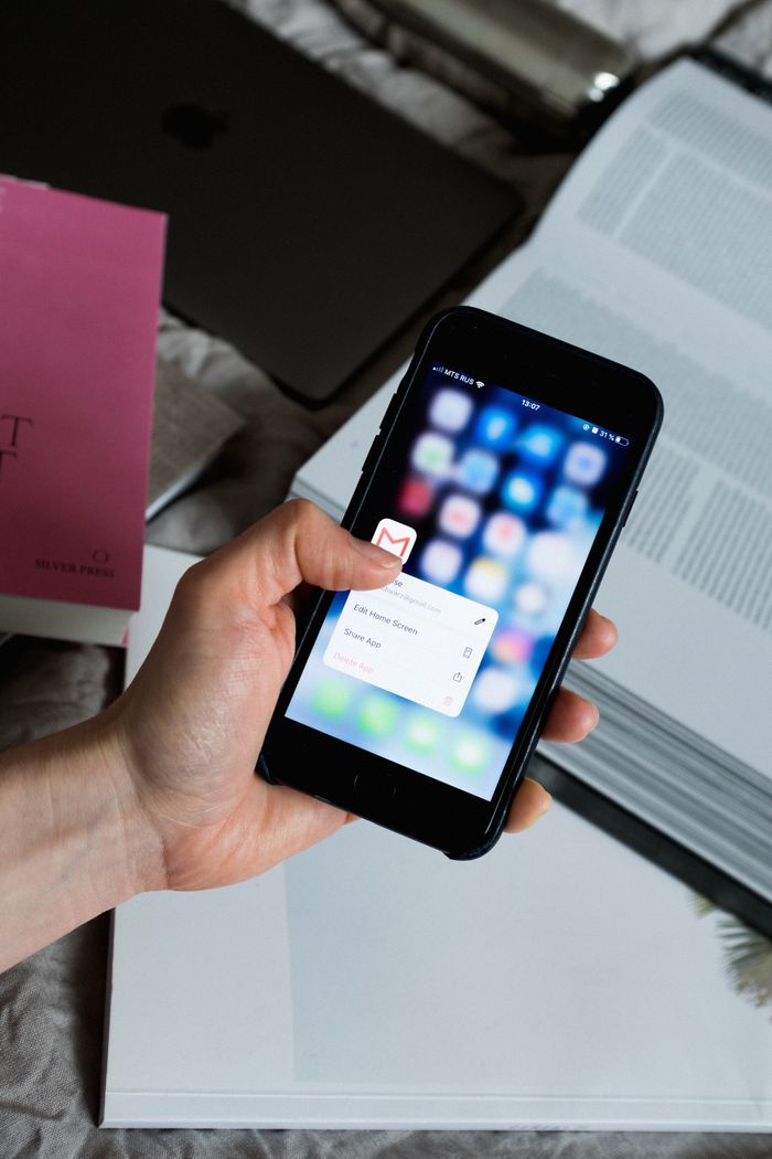 about-01 Hand holding smartphone with email app open, surrounded by books and laptop.